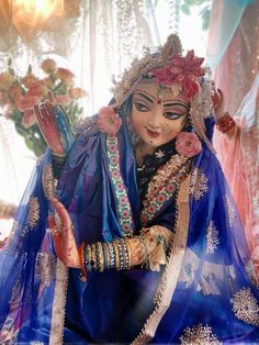 a woman dressed in blue and gold sitting on top of a bed next to flowers