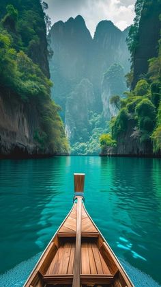 a wooden boat floating on top of a lake surrounded by mountains and greenery in the distance