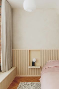 a bed sitting next to a window in a bedroom under a light fixture on top of a wooden floor