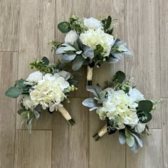 three bridal bouquets with white flowers and greenery laid out on the floor