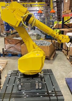 a yellow robot is sitting on top of a piece of metal in a warehouse with other boxes