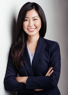 a woman with her arms crossed standing in front of a white wall wearing a black blazer