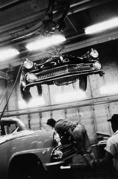 two men working on an old car in a garage while another man looks at it