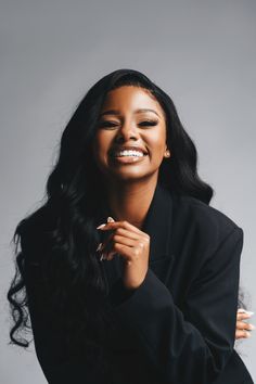 a woman with long black hair smiling and posing for the camera in front of a gray background