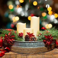 two white candles sitting on top of a metal tray with pine cones and poinsettis