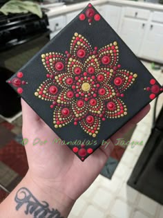 a hand holding up a small black box with red and yellow designs on it