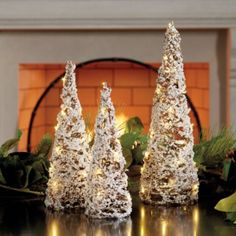 three white christmas trees sitting on top of a table next to a fireplace in a living room