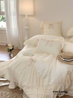 a white bed in a bedroom next to a window with curtains and pillows on it