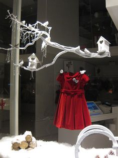 a red dress is hanging on a branch in front of a glass window with snow