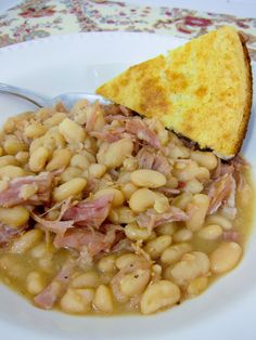 a white plate topped with beans and ham next to a piece of toasted bread