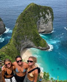 three women posing for a photo in front of the ocean and two large rock formations