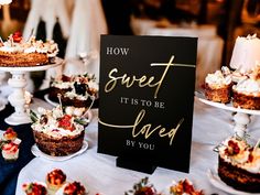 a table topped with cakes and desserts on top of white tables covered in black paper