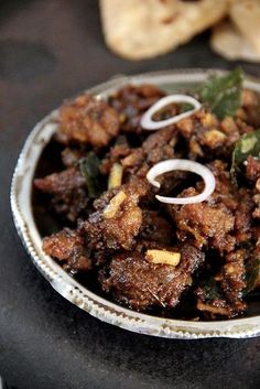 a bowl filled with meat and onions on top of a black table next to pita bread