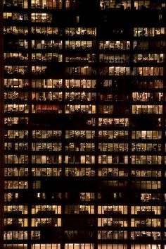 black and white photograph of many windows in a building at night with the lights on