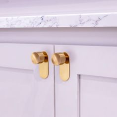 two brass handles on white cabinets in a bathroom