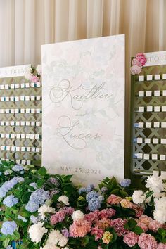 a sign that is on top of some flowers and greenery in front of two chairs