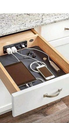 an open drawer in the middle of a kitchen counter with electronics inside and charging on it