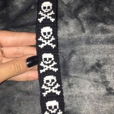 a woman's hand holding a black and white knitted bracelet with skulls on it