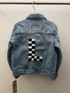 a denim jacket with the letter i on it hanging from a hook in front of a white wall