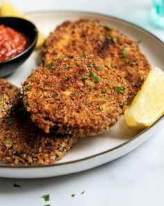 three crab cakes on a plate with lemon wedges and ketchup