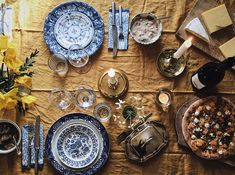 the table is set with plates, silverware and flowers in blue and white dishes