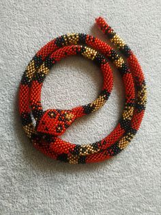 a red and black beaded bracelet with an orange cat on the clasp, sitting on a white surface