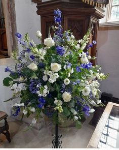 a vase filled with white and blue flowers sitting on top of a marble floor next to a clock