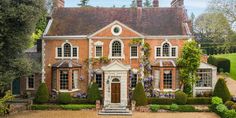 a large brick house with lots of windows and plants on the front lawn, surrounded by hedges