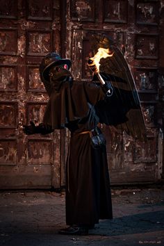 a man dressed as an angel holding a flame in one hand and a black bird on the other