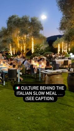 people sitting at tables in the middle of an open field with trees and lights behind them