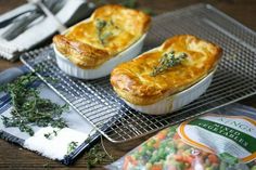 two pies sitting on top of a cooling rack next to some vegetables and seasoning