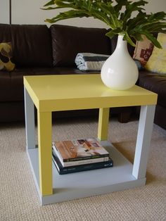 a yellow end table with magazines on it in front of a couch and coffee table