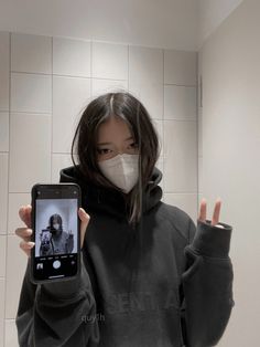 a woman wearing a face mask holding up a cell phone