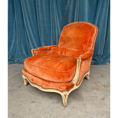 an orange chair sitting on top of a cement floor next to a blue curtained wall