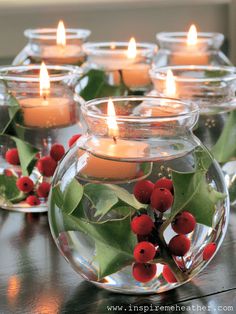 candles are lit in glass bowls with holly and berries