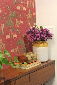 a vase with flowers sitting on top of a wooden table next to a wall paper