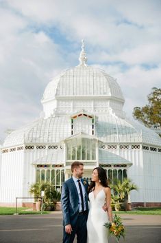 a bride and groom standing in front of a large glass building with a domed roof