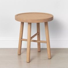 a small wooden stool sitting on top of a hard wood floor next to a white wall