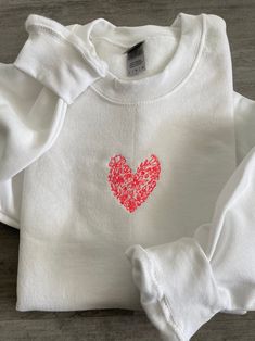 a white shirt with a red heart embroidered on the chest and sleeves, sitting on a wooden surface