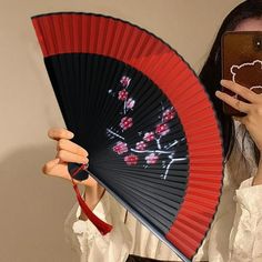 a woman holding up a red and black fan with cherry blossoms on it's side