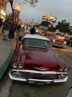 an old car is parked on the side of the road in front of some people