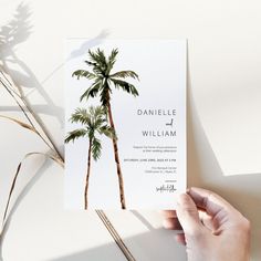 a person holding up a wedding card with palm trees on it