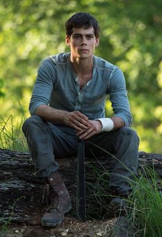 a young man sitting on top of a tree trunk holding a knife in his hand