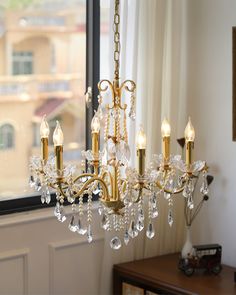 a gold chandelier with crystal drops hanging from it's arms in front of a window