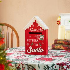 a red house shaped mailbox sitting on top of a table next to a christmas tree