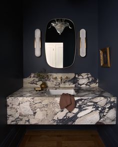 a bathroom with marble counter tops and gold fixtures on the wall, along with an oval mirror