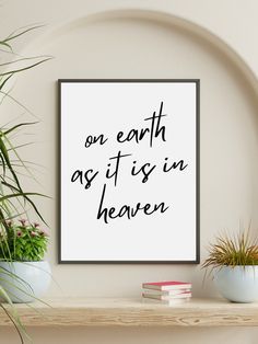 a framed poster with the words on earth as it is in heaven next to potted plants