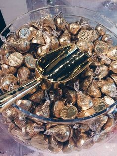 a glass bowl filled with lots of gold coins and a scoop full of chocolates