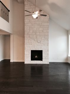 an empty living room with white brick fireplace and dark wood flooring in the middle