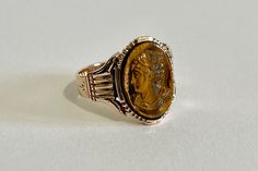 "Gorgeous 10k rosey gold Mid Victorian Era ring featuring an intricately carved tigers eye cameo. The bezel set cameo depicts a lovely lady facing to the left side, with her hair in a fancy up-do with a ribbon. A bezel setting secures the genuine cameo. Intricate details makes up the entire setting! Beautiful piece of fine vintage cameo jewelry, circa 1886-1910s!  ERA - Circa 1886 - 1910 Mid Victorian Era METAL / MATERIAL - 10k rosey gold, carved tigers eye MARKINGS / HISTORY -Hand engraved \" March 8th\" with an anchor CONDITION - Good antique condition. Cameo is in very nice shape, and secure. The setting's details have been beautifully preserved, may have been resized since the full date is missing. Incredible cameo ring! SIZE / MEASUREMENTS - Size: 7 1/2 ,Ring head height: 15.9 mm, Bac Eye Markings, Vintage Cameo Jewelry, Cameo Jewelry, Cameo Ring, Vintage Cameo, Tigers Eye, Metal Material, Hand Engraving, Victorian Era